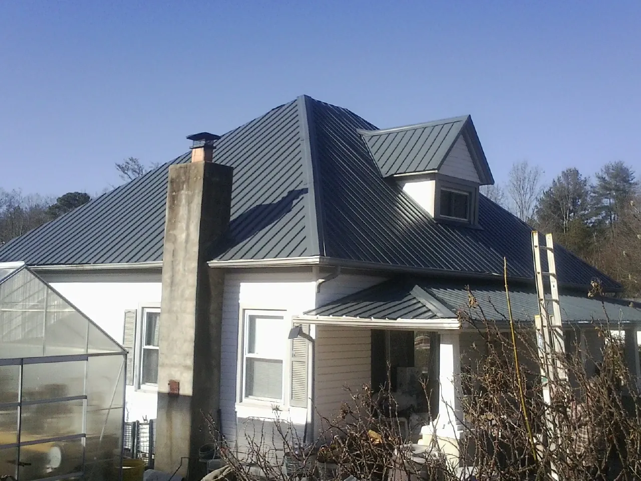 Dark blue standing seam metal roof on a white farmhouse with dormer — Slate & Tile Roof Repair by Roofing Brothers in Mission Hill