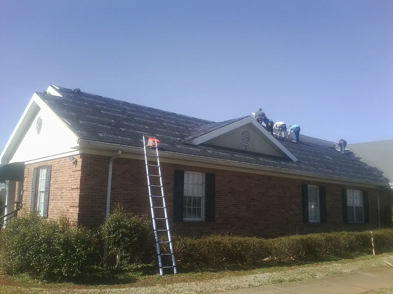 Crew tearing shingles off a brick ranch roof with a ladder set — Metal Roof Repair work by our crew in Mission Hill
