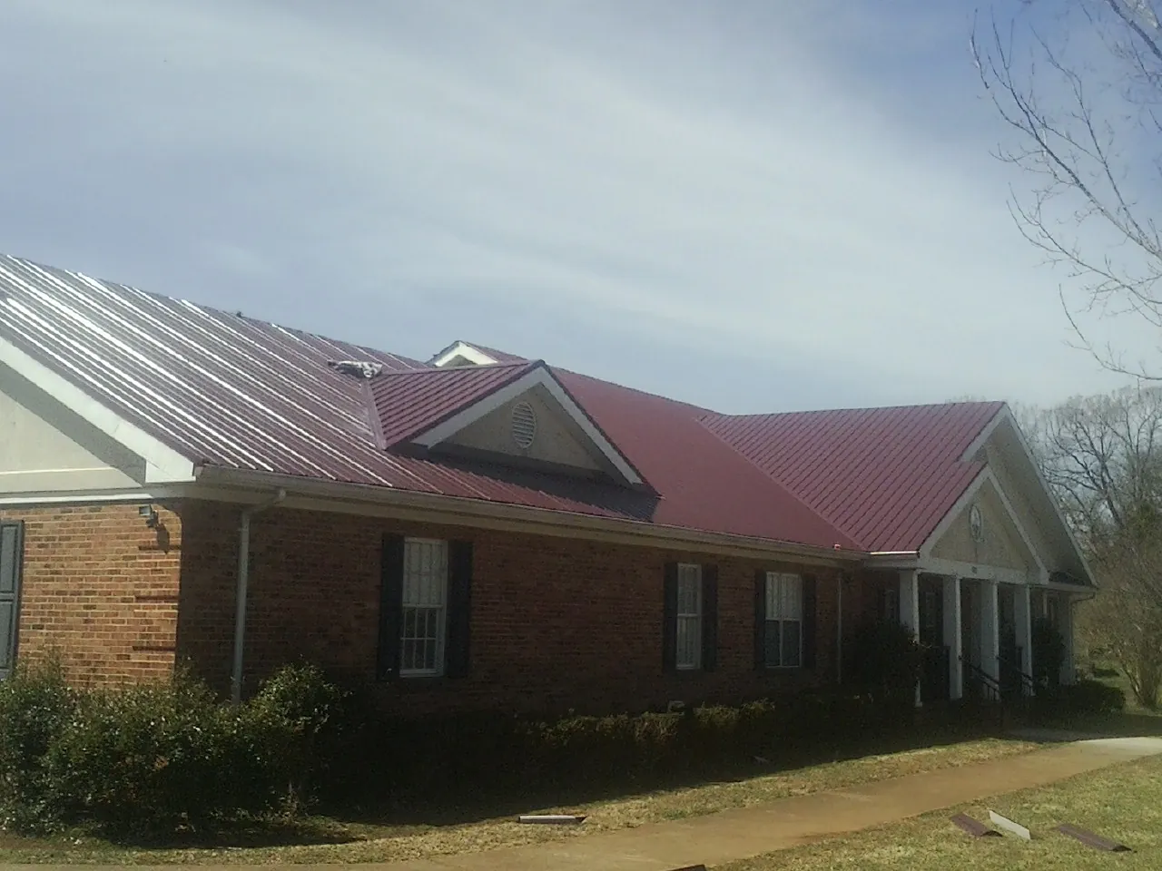 Red metal roof with gabled entries on a long brick building, from a Hail Damage Roof Repair job in Mission Hill