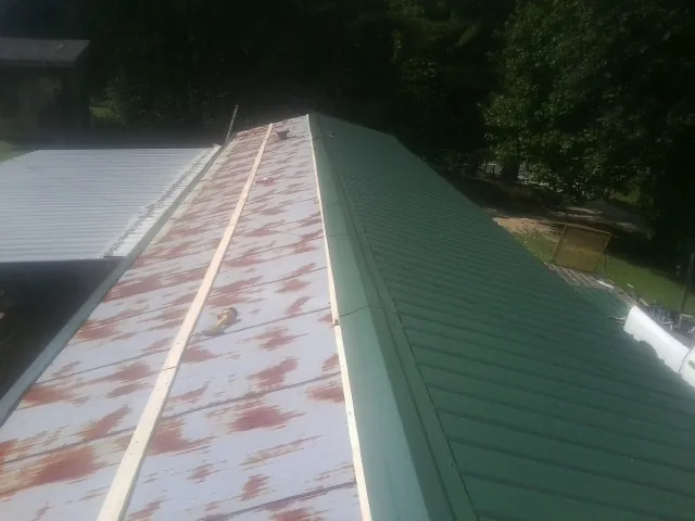 Old rusted panels beside newly installed green metal roofing — Wind Damage Roof Repair by Roofing Brothers in Mission Hill