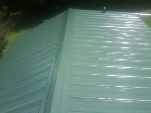 New green metal panels meeting at the ridge of a roof — Flat Roof Repair work by our crew in Mission Hill