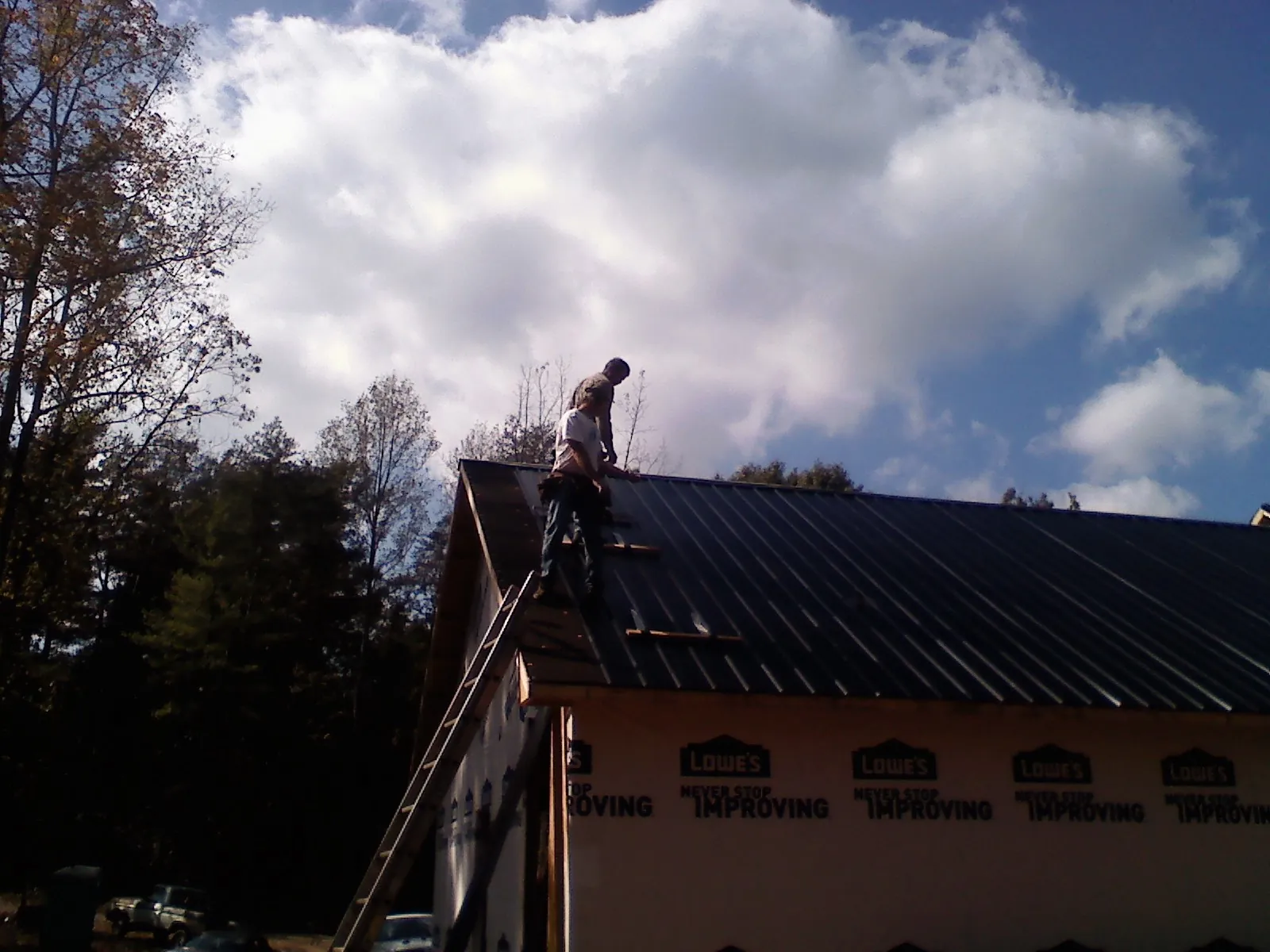 Roofer fastening dark metal panels high against a cloudy sky, from a Roof Inspection job in Mission Hill
