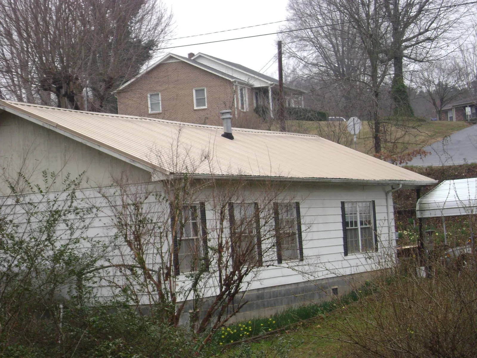 Tan metal roof on a white sided house set into a hillside — Commercial Roofing by Roofing Brothers in Mission Hill