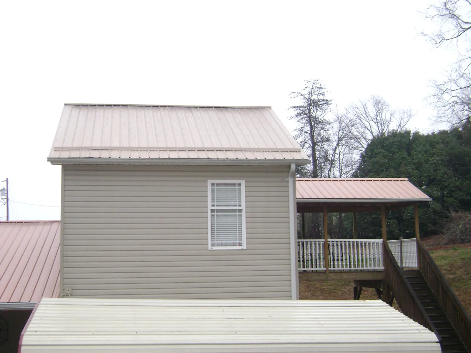 Tan metal roofs on a two story addition and attached porch, from a Roof Replacement job in Mission Hill